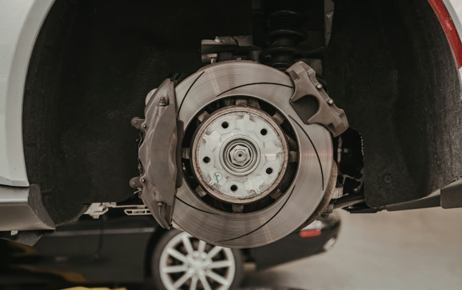 Slotted brake rotor and caliper on a lifted car during brake service at Action Automotive in Colorado Springs